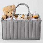 Gray storage caddy with baby items including a teddy bear, bottles, and toys on a light gray background