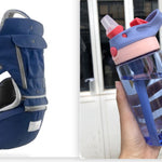 Navy baby carrier and blue water bottle with pink lid held by a hand.