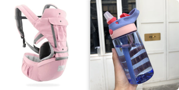 Pink baby carrier and blue water bottle with red lid held by a hand against a blurred background.