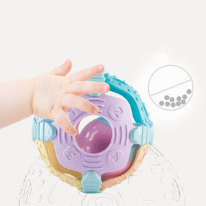 Colorful baby teething ring with a hand reaching towards it on a light gray background