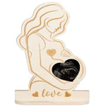 Wooden ornament of a pregnant woman holding a heart-shaped frame with 'love' engraving on a white background.