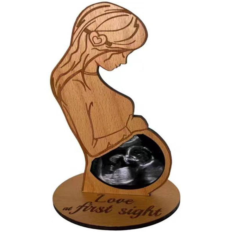 Wooden sculpture of a woman holding an ultrasound image with 'Love at first sight' text.