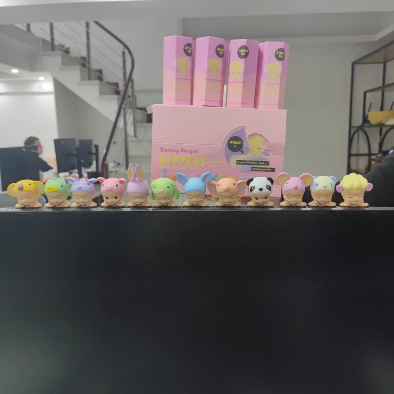 Row of colorful plush toys in front of pink boxes on a black surface.