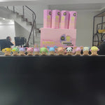Row of colorful plush toys in front of pink boxes on a black surface.