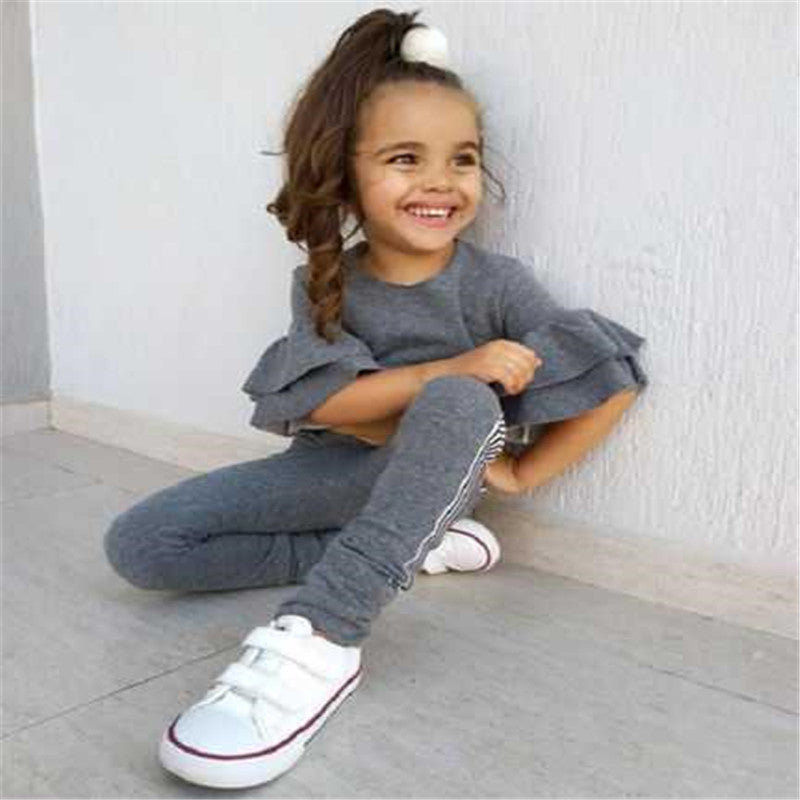 Child sitting on the floor wearing a gray outfit with white sneakers.