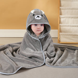 Baby wrapped in a gray hooded towel with bear design on a wooden floor.