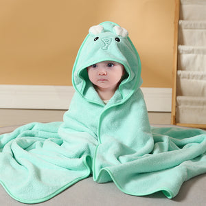 Child wearing a green hooded towel with a cartoon character on a beige couch.