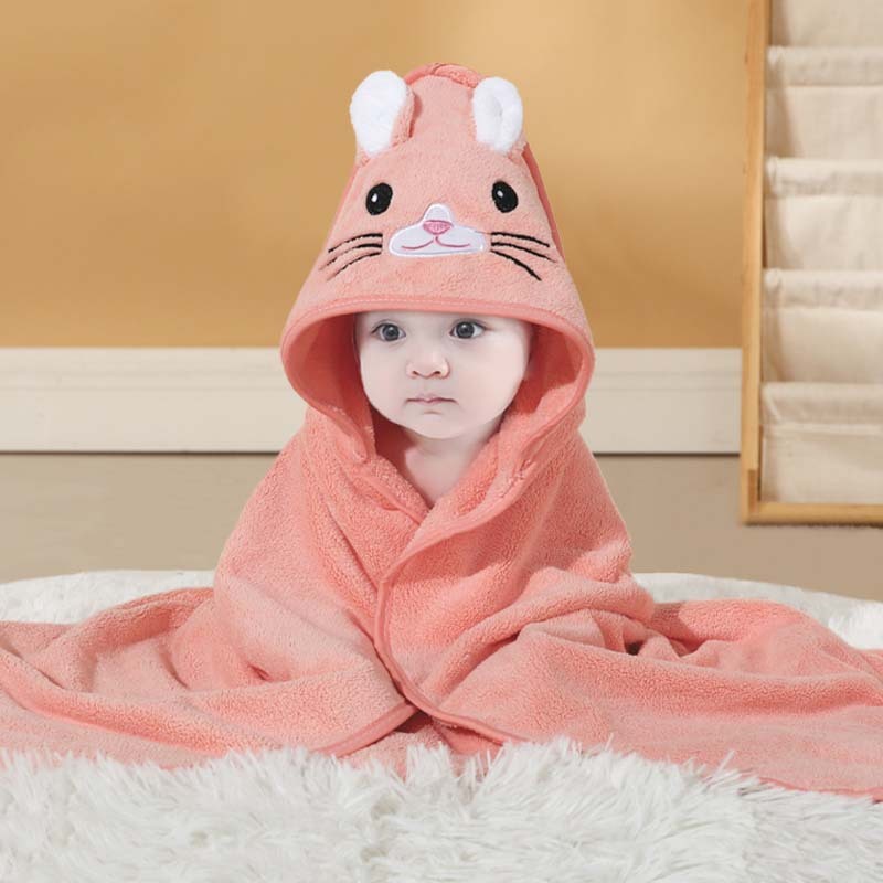 Baby wrapped in a pink hooded towel with animal face design on a white surface.