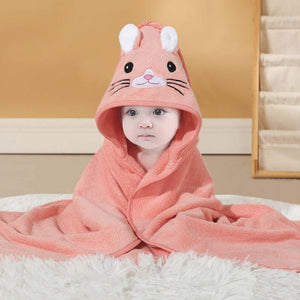Baby wrapped in a pink hooded towel with animal face design on a white surface.