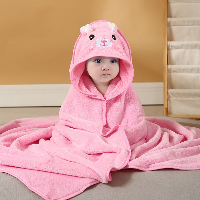 Baby wrapped in a pink hooded towel with bear ears and face, sitting on a beige surface.