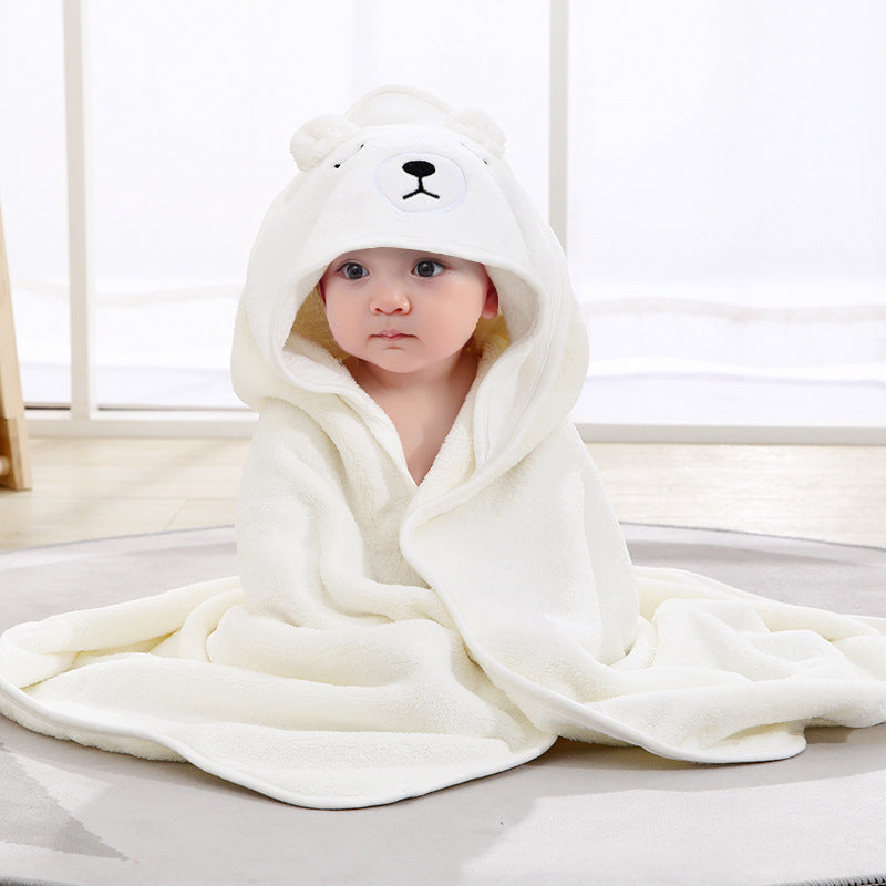 Baby wrapped in a white bear hooded towel on a light wooden floor.
