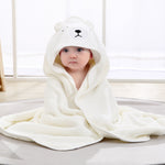 Baby wrapped in a white bear hooded towel on a light wooden floor.