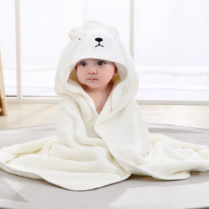 Baby wrapped in a white bear hooded towel on a light wooden floor.