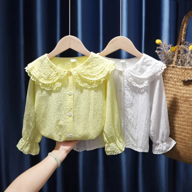 Yellow and white lace blouses on hangers against a dark blue curtain background.