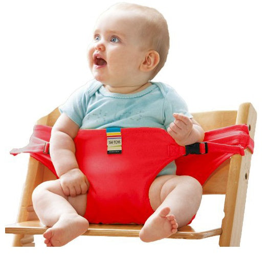 Baby sitting in a red baby seat on a wooden chair with a white background