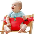 Baby sitting in a red baby seat on a wooden chair with a white background