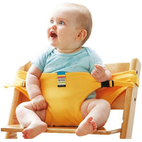 Baby sitting in a yellow safety seat on a wooden chair with a white background
