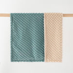 Two textured towels, one green and one beige, hanging on a wooden rod against a white background.