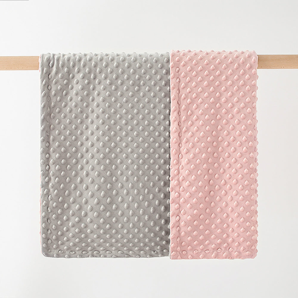 Two textured baby blankets, one gray and one pink, on a wooden rod against a white background.