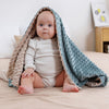 Baby sitting on a bed with a textured blanket draped over them
