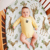 Baby in a yellow onesie with a bee design lying on a crib mattress with giraffe and leaf pattern.