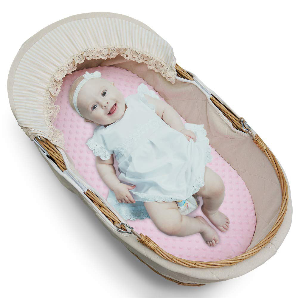 Baby in a Moses basket with pink bedding and white headband
