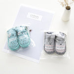 Two sets of baby socks in clear packaging on a white surface with a 'Cereal' box in the background.