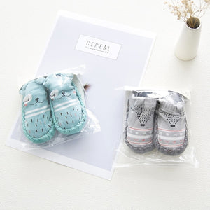 Two sets of baby socks in clear packaging on a white surface with a 'Cereal' box in the background.