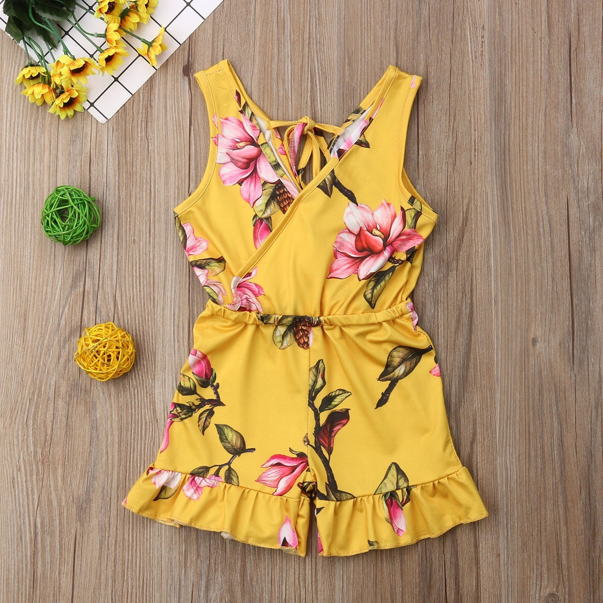 Yellow romper with floral pattern on a wooden surface