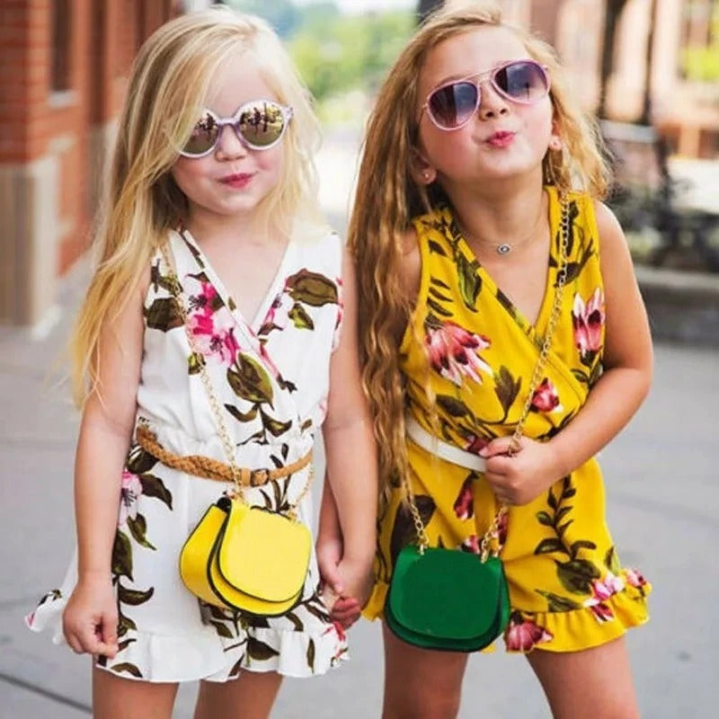 Two young girls in floral outfits with colorful handbags on a street.