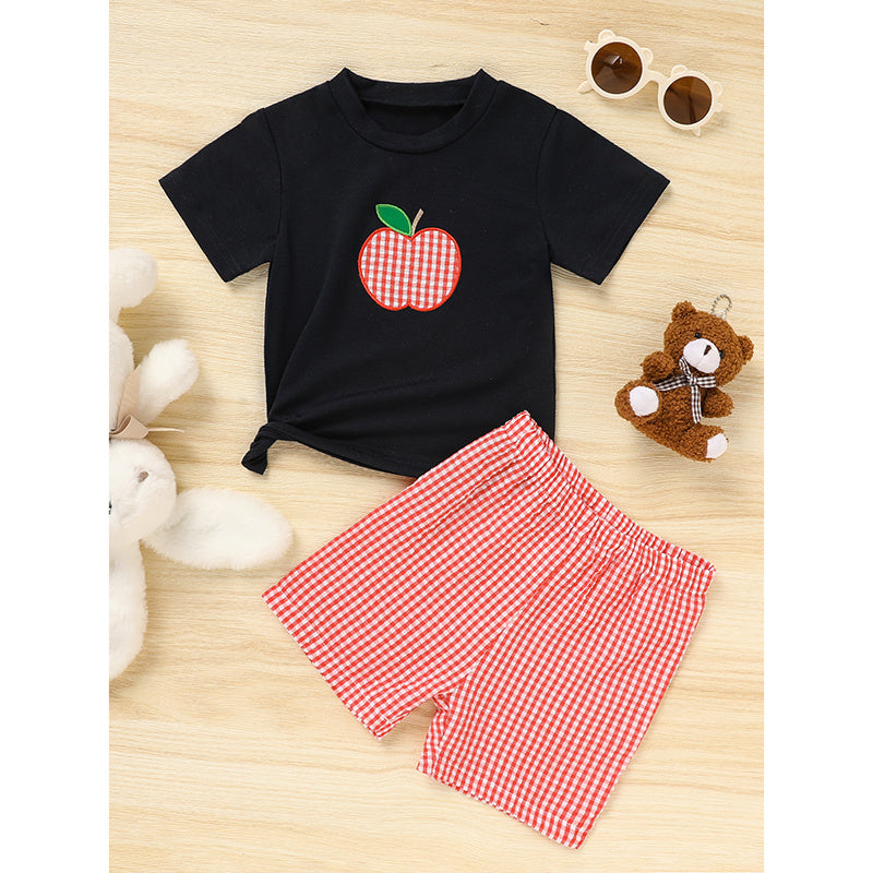 Black t-shirt with a red apple design and red checkered shorts on a wooden surface.