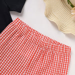 Red and white checkered pants on a white surface with a straw hat and black shirt in the background.