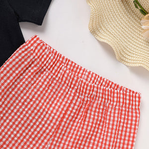 Red and white checkered pants on a white surface with a straw hat and black shirt in the background.