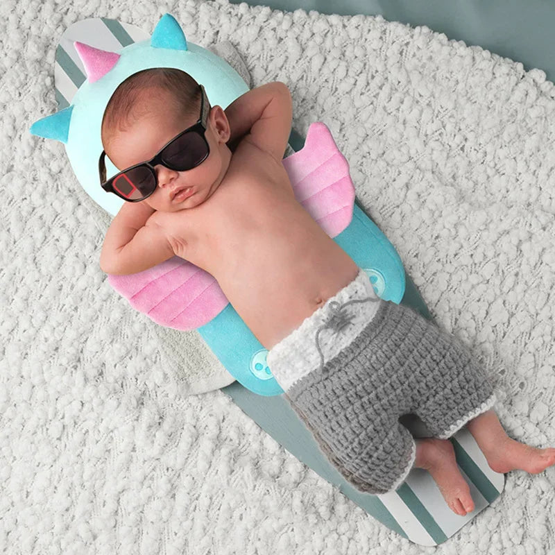 Baby lying on a colorful inflatable shark toy wearing sunglasses and gray pants.
