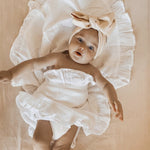 Baby in a white outfit with a bow on a beige background