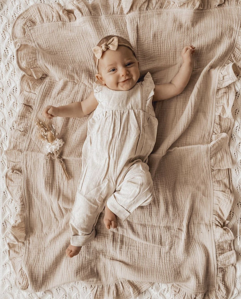 Baby in a white outfit lying on a textured beige blanket