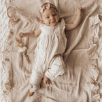 Baby in a white outfit lying on a textured beige blanket