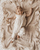 Baby in a white outfit lying on a textured beige blanket