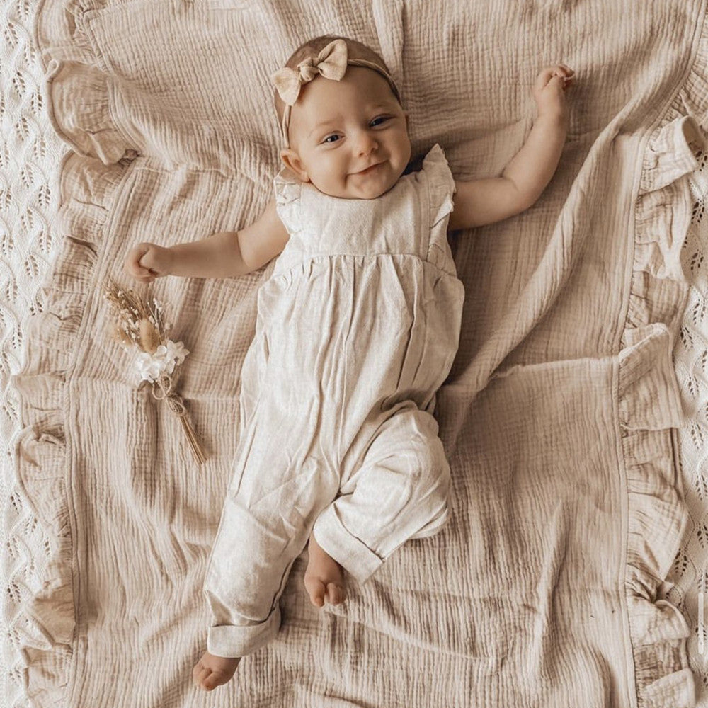 Baby in a white romper lying on a textured blanket
