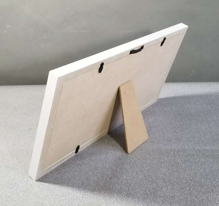 White picture frame with a cardboard stand on a gray surface