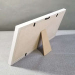 White picture frame with a cardboard stand on a gray surface