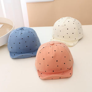 Three polka dot baseball caps in blue, pink, and white on a light surface.
