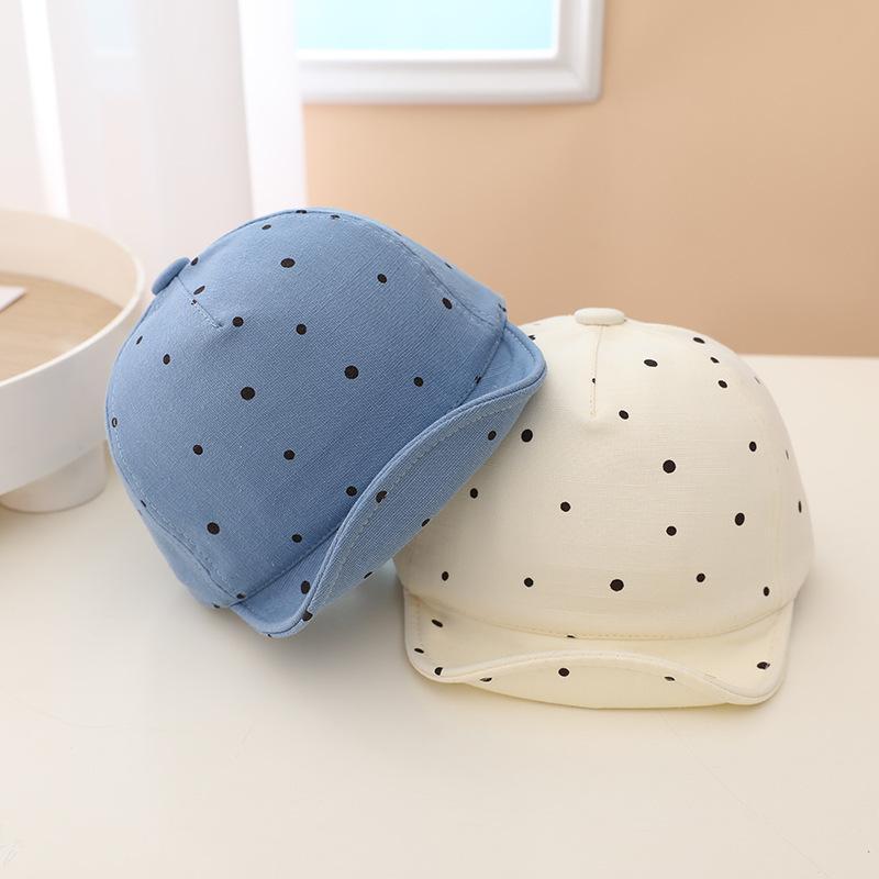 Two baby hats with polka dot patterns, one blue and one white, on a light surface.