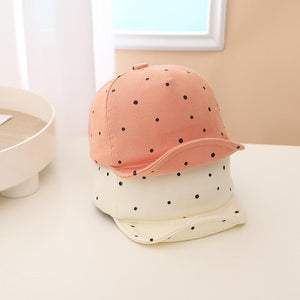 Pink and white polka dot baby hat on a white surface with a neutral background