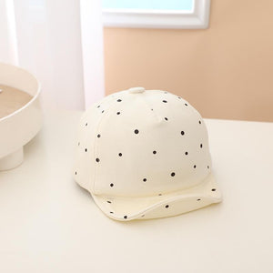 White baby hat with black polka dots on a light surface