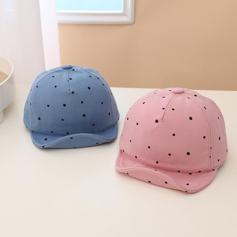 Two children's baseball caps, one blue and one pink, with black polka dots on a white surface.