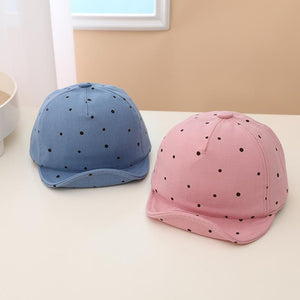 Two children's baseball caps, one blue and one pink, with black polka dots on a white surface.
