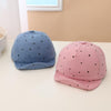 Two children's baseball caps, one blue and one pink, with black polka dots on a white surface.