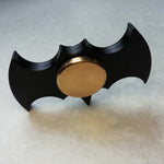 Black and gold fidget spinner shaped like a bat emblem on a light gray background