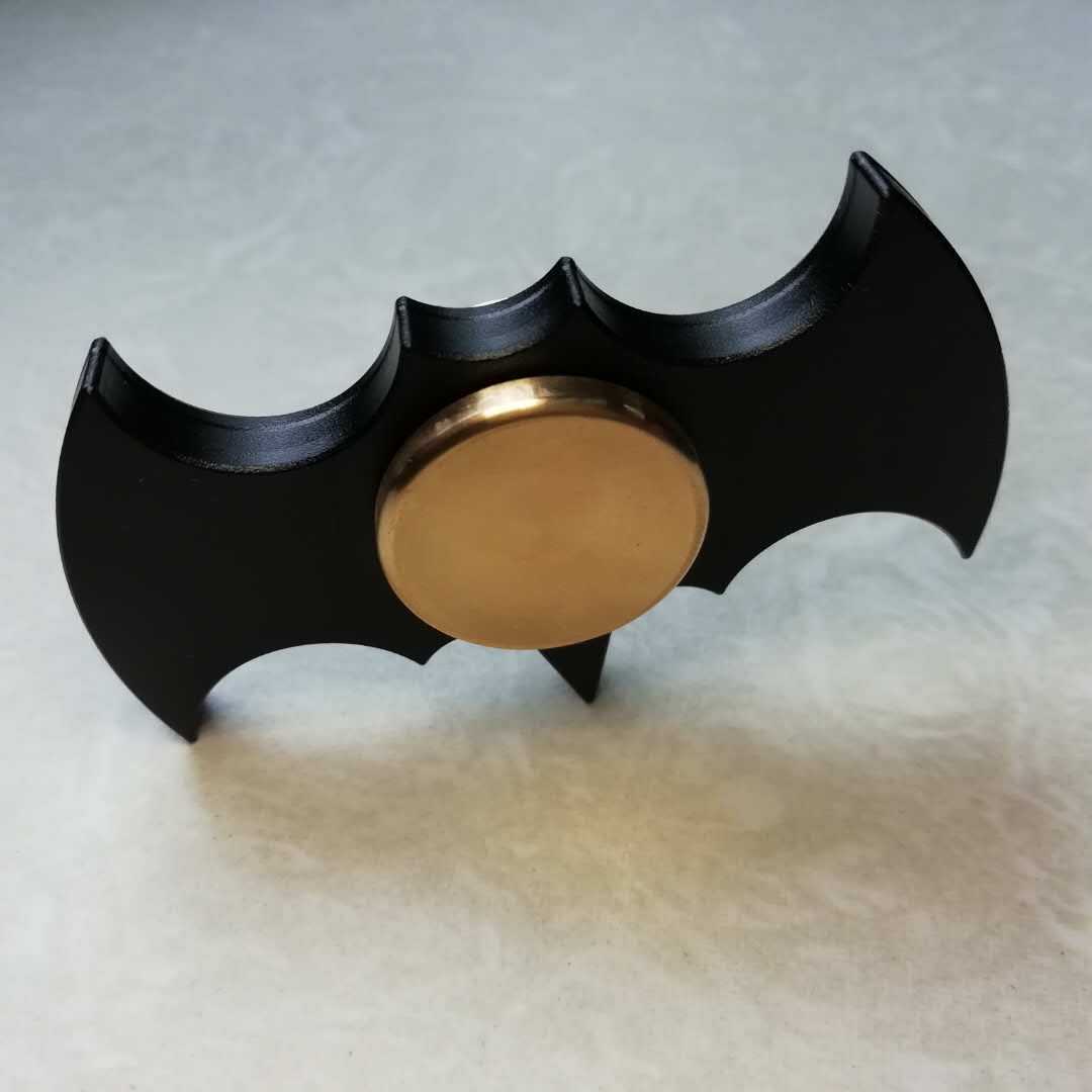 Black and gold fidget spinner shaped like a bat emblem on a light gray background